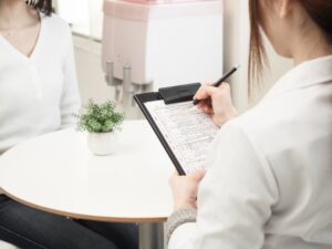 カウンセリングを受ける女性と問診表を記入する女性スタッフ